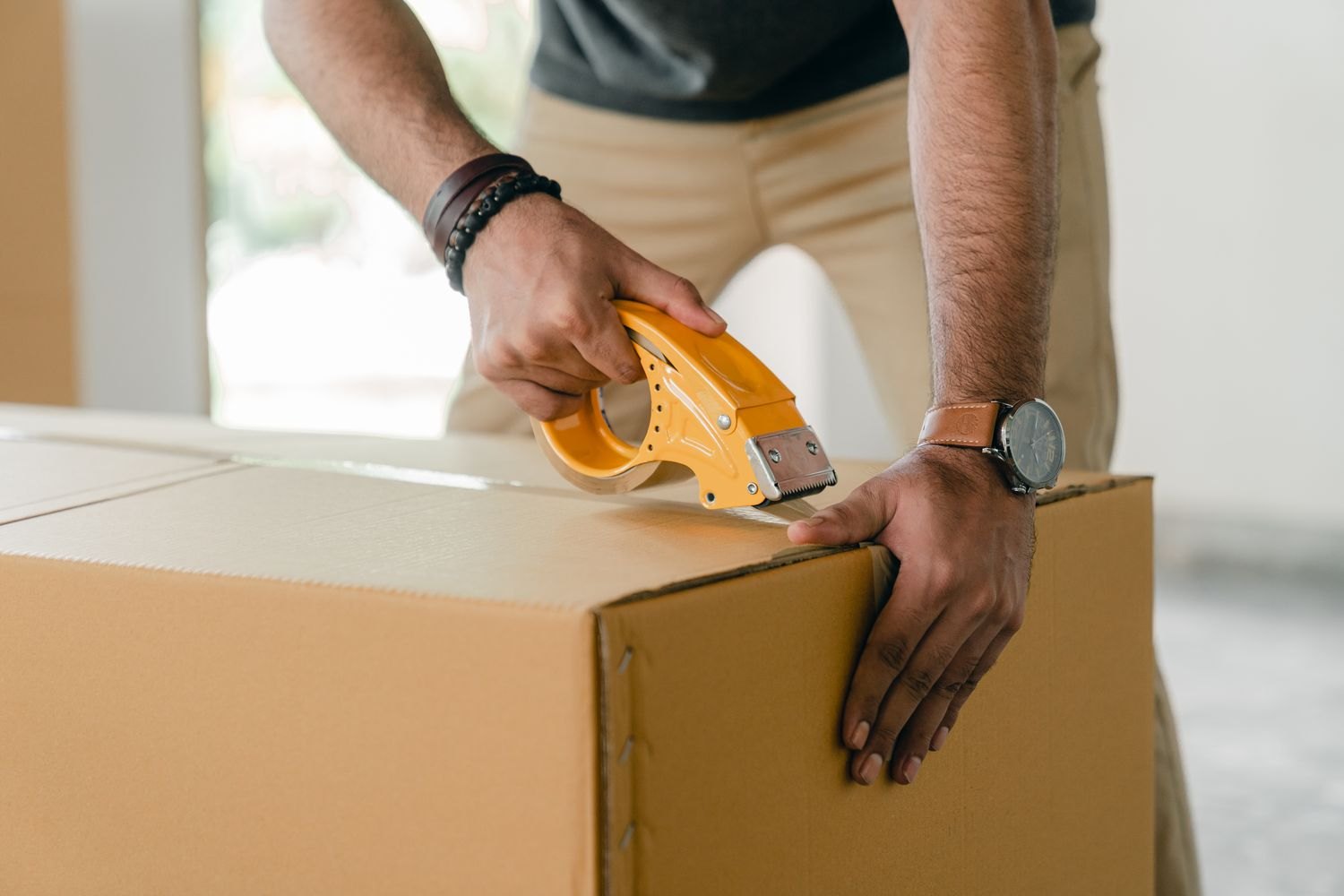 Hands sealing a box with a packing tape dispenser